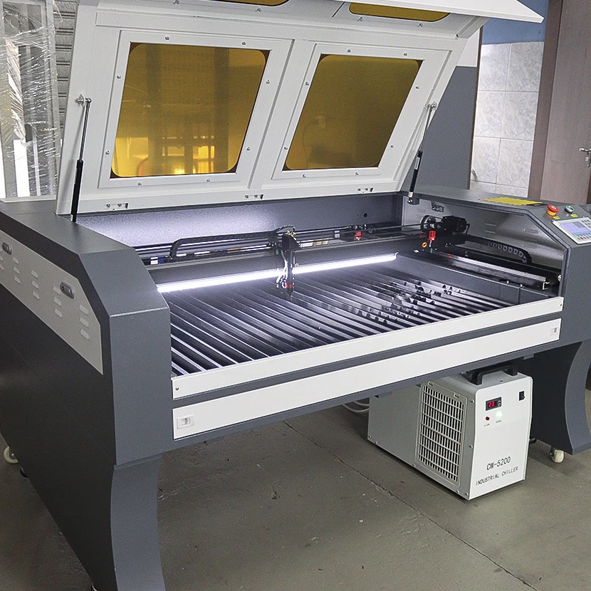 Visão frontal de uma máquina de corte a laser CNC industrial com tampa aberta e iluminação interna ativa, exibindo o chiller CW-5200 posicionado na parte inferior.